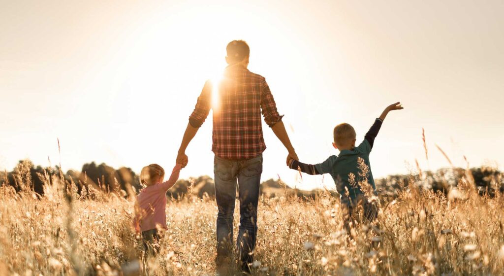 Father waking with two children at sunset on a grassy hill